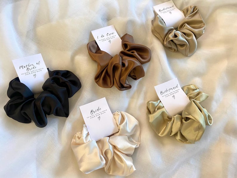 May include: Set of six satin scrunchies in various colors with matching cards that say "Bride", "Mother of the Bride", "Maid of Honor", "Bridesmaid", and "Bridesmaid".