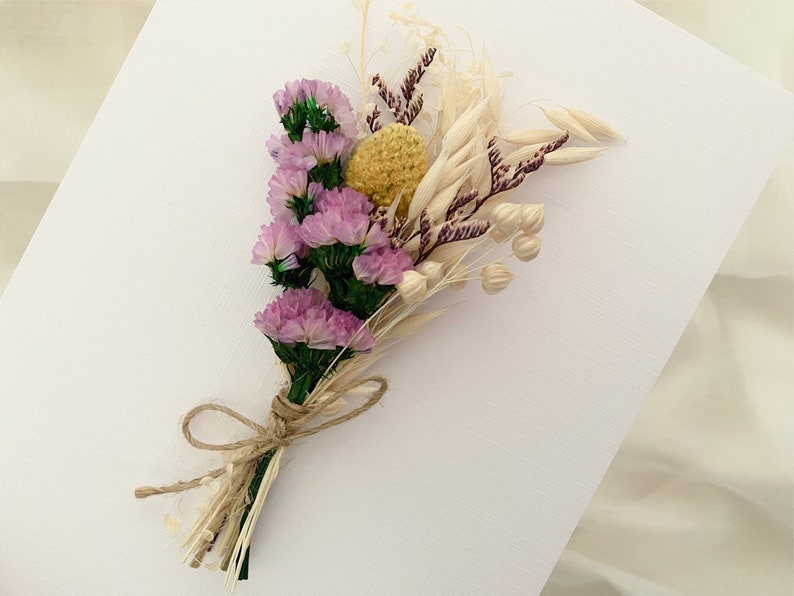 Op de afbeelding: Een klein boeket gedroogde bloemen gebonden met touw. Het boeket bevat paarse statice, gele billy buttons en gedroogde grassen.
