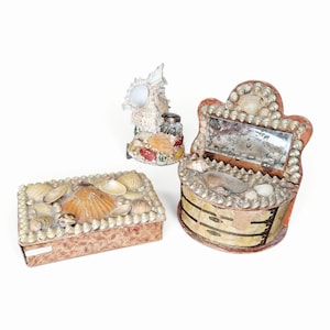 May include: A rectangular box, a small shell-encrusted figurine, and a semi-circular vanity organizer, all decorated with various natural seashells. The vanity organizer features a small rectangular mirror and a curved front with gold-toned accents.