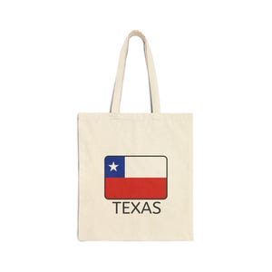 May include: A cream-coloured tote bag with a rectangular design featuring the Texas flag and the word "TEXAS" in black. The flag design includes a blue star, white, and red stripes.