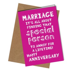 May include: A magenta anniversary card with white text that reads "MARRIAGE IT'S ALL ABOUT FINDING THAT special person TO ANNOY FOR A LIFETIME! Happy ANNIVERSARY" is displayed on top of a brown envelope.