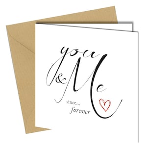 May include: A white card with the words "you & Me" in black script, a red heart, and the words "since... forever". The card is accompanied by a brown envelope.