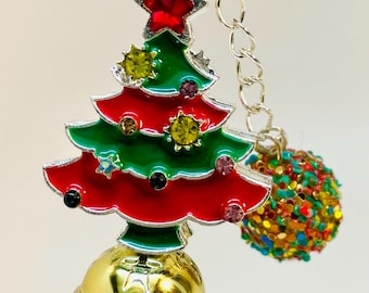May include: A festive Christmas pen with a red barrel adorned with stars, holly, and colorful dots. The pen features a gold bell-shaped base, a green and red Christmas tree charm, and a dangling, multi-colored ornament. The pen is approximately 6 inches long.