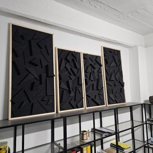 以下が含まれることがあります： 白い壁に取り付けられた、幾何学的な形状の黒い音響パネルが4つ。各パネルは明るい木材で縁取られています。パネルはサイズが異なり、黒い金属製の棚の上に一列に並んでいます。