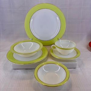 May include: A collection of white and chartreuse dinnerware. The set includes a large plate, bowls, saucers, and a teacup with a matching saucer. Each piece has a chartreuse border with a gold trim.