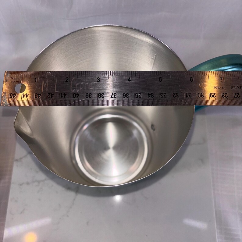 May include: A stainless steel pitcher with a teal handle. The pitcher is approximately 6 inches in diameter. The pitcher has a spout for easy pouring.