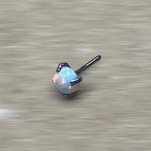 May include: A small, white opal gemstone set in a silver prong setting. The opal is a light blue color with a hint of pink.