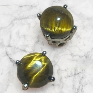 May include: A pair of gold tiger's eye gemstone earrings with silver settings. The earrings are round and have a smooth, polished finish.