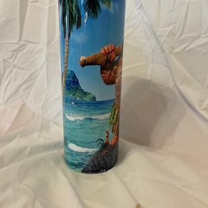K&ouml;nnte beinhalten: Ein hoher, rostfreier Becher mit einem bunten Bild eines Zeichentrickcharakters aus dem Film Vaiana. Das Bild zeigt eine tropische Inselszene mit Palmen, Ozeanwellen und einem Hahn.
