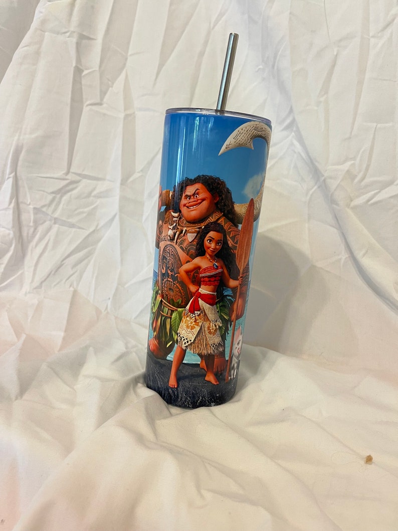 K&ouml;nnte beinhalten: Ein Edelstahlbecher mit blauem Hintergrund und einem Motiv von Maui und Moana aus dem Disney-Film Vaiana. Der Becher hat einen Strohhalm.