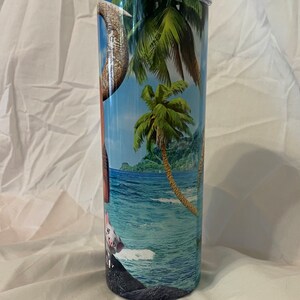 K&ouml;nnte beinhalten: Ein Edelstahlbecher mit einer tropischen Strandkulisse mit Palmen, blauem Wasser und einem Schwein. Der Becher hat einen durchsichtigen Deckel.