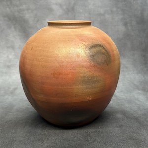 Peut inclure: Un vase rond en céramique de couleur terre cuite, avec un corps large et un col étroit. Le vase a une finition lisse et mate avec des variations de couleur, notamment des nuances d'orange, de marron et de noir. Poterie décorative.