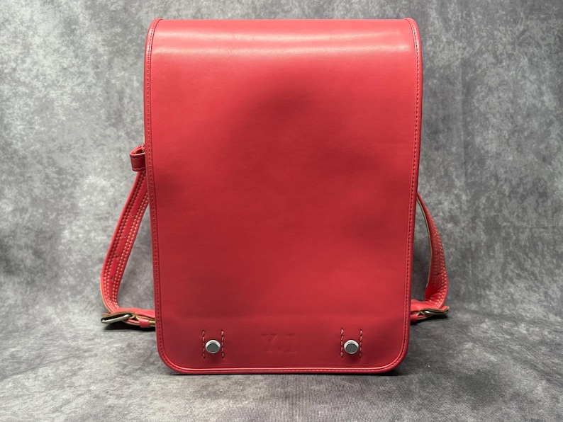 May include: A bright pink leather satchel with a flap closure and adjustable shoulder strap. The bag has silver hardware and a minimalist design.