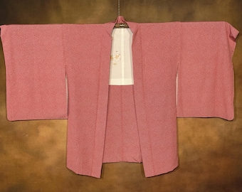 Puede incluir: Un kimono japonés rosa con forro blanco y un pequeño diseño bordado. El kimono está hecho de una tela suave y ligera y tiene un estilo tradicional.
