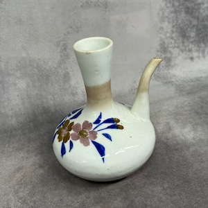 May include: A white ceramic sake bottle with a brown glaze and blue and gold floral designs.