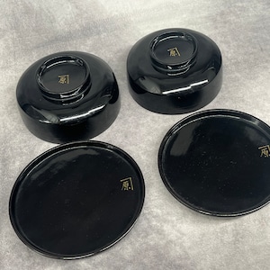 以下が含まれることがあります： 金色の文字が書かれた黒い漆器のボウルが4つ。ボウルは丸く、わずかに縁があります。ボウルに書かれた文字は「原」です。