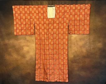 May include: A traditional Japanese kimono with a geometric pattern of orange and brown stripes. The kimono is made of a soft, silky fabric and has a square neckline.