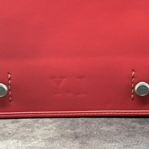 May include: Close-up of a red leather bag with silver metal accents and the letters "YI" embossed on the front.