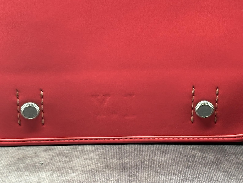 May include: Close-up of a red leather bag with silver metal accents and the letters "YI" embossed on the front.