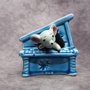May include: A blue ceramic piano figurine with a white mouse peeking out of the top. The piano has a detailed design and is a charming decorative piece.