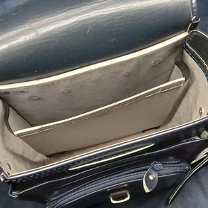 May include: A black leather backpack with multiple compartments and a zippered pocket. The backpack is open and the interior is lined with a beige fabric.