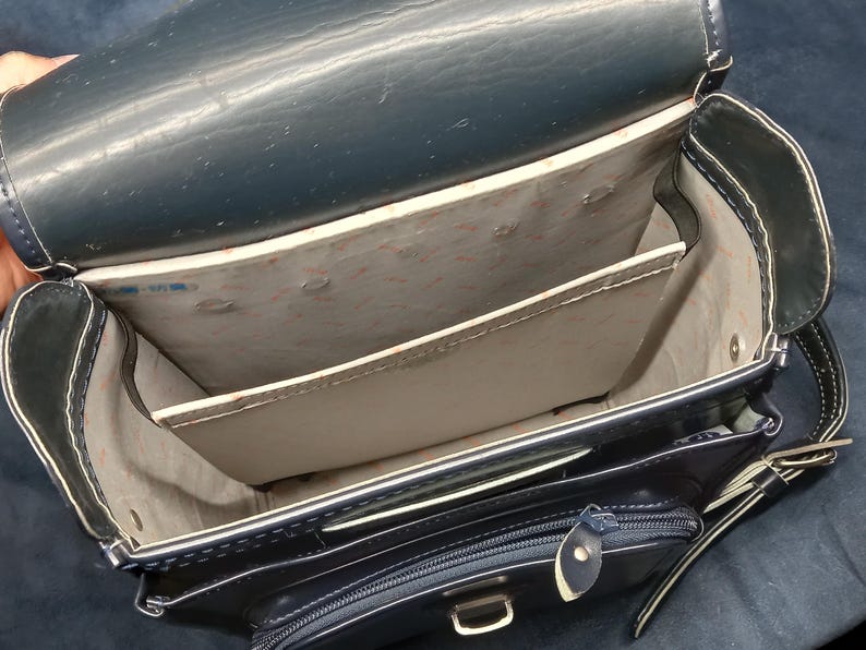 May include: A black leather backpack with multiple compartments and a zippered pocket. The backpack is open and the interior is lined with a beige fabric.