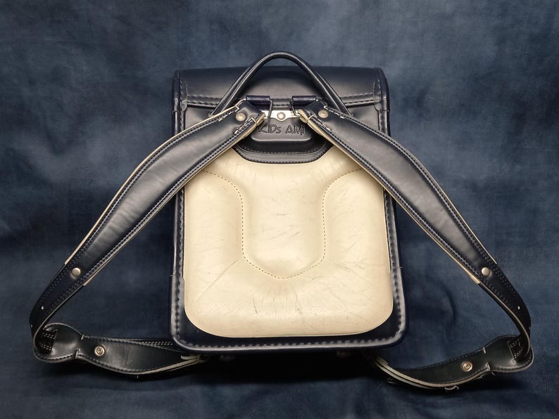 May include: A black leather backpack with a white leather front panel and silver hardware. The backpack has two adjustable straps and a top handle.