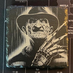May include: Black and white illustration of Freddy Krueger, a horror movie character, with a striped background. He is wearing a brown fedora hat and a glove with blades.