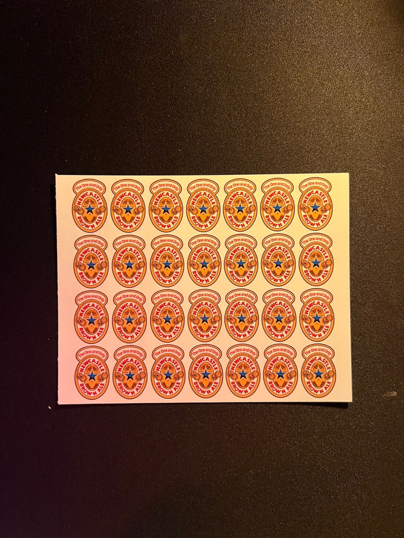 May include: A sheet of 36 stickers featuring the Newcastle Brown Ale logo. Each sticker is round and features a brown ale bottle with a red and white label that says "The One and Only Newcastle Brown Ale".