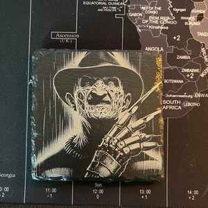 May include: Black and white illustration of a horror movie character with a knife. The character is wearing a hat and has a menacing expression.