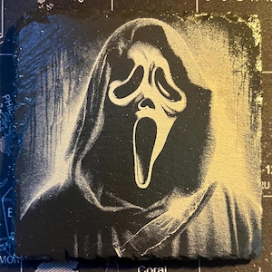 May include: A black and white image of the Ghostface character from the Scream movie franchise. The character is wearing a white mask with a scream face and a black hooded robe. The character is holding a knife in their right hand.