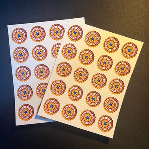 May include: Two sheets of white paper with multiple stickers of a red, yellow, and blue logo that reads "Newcastle Ale - 317" in a circle.