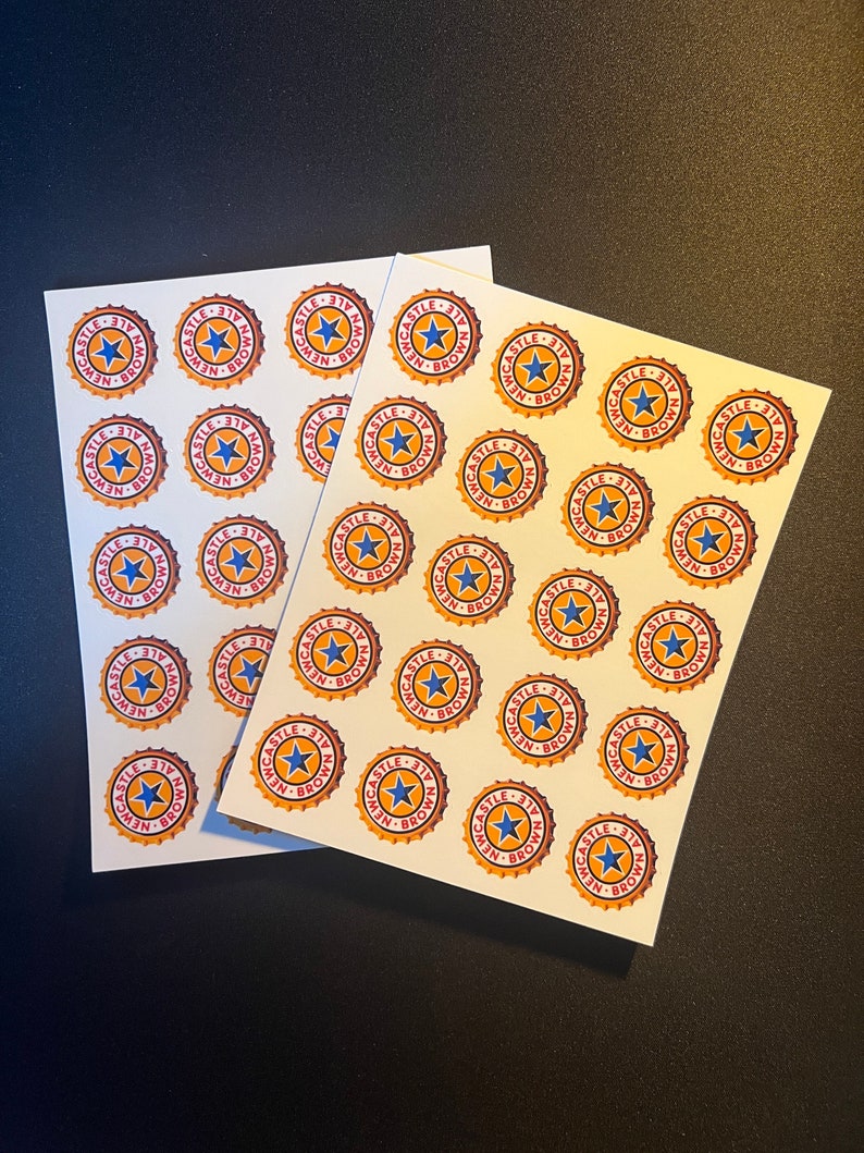 May include: Two sheets of white paper with multiple stickers of a red, yellow, and blue logo that reads "Newcastle Ale - 317" in a circle.