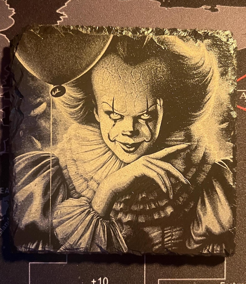 May include: Black and white illustration of Pennywise the Dancing Clown from the movie IT. The clown is wearing a ruffled collar and has a sinister smile. A red balloon is floating above the clown's head.