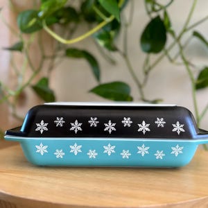 May include: A blue and black casserole dish with a snowflake design. The dish is made of ceramic and has a lid.