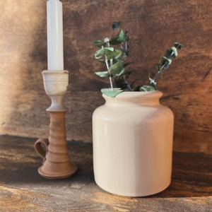 May include: A white ceramic candle holder with a twisted design and a white candle. A small, off-white ceramic vase with a sprig of green eucalyptus.