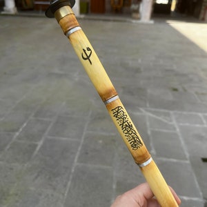 Może przedstawiać: Tradycyjny flet trzcinowy, czyli ney, z metalową nasadką i ozdobnymi opaskami. Bambusowy instrument posiada wytrawioną kaligrafię i symbol. Ney to instrument dęty używany w muzyce bliskowschodniej.