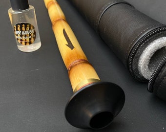 May include: A traditional wind instrument, a zurna, made of light brown wood with a black bell and a black case. A small bottle with a black cap and a label is also present.