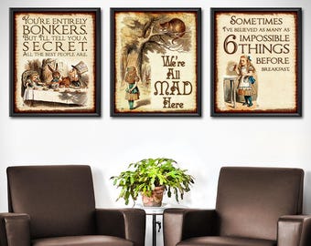 May include: Three framed vintage-style Alice in Wonderland prints. The prints feature quotes and illustrations from the story, including the Mad Hatter's tea party, the Cheshire Cat, and Alice. The frames are black, and the prints have a distressed, aged appearance.