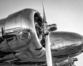 May include: A vintage airplane with a shiny silver finish and a large propeller. The airplane is in black and white.