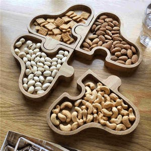 May include: A wooden puzzle-shaped serving tray with four compartments. The tray is filled with different types of nuts, including almonds, pistachios, and cashews.