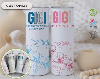 Può includere: Due bicchieri bianchi in acciaio inossidabile con disegni floreali e la parola "GIGI" in blu e rosa. Il bicchiere blu ha nomi sotto la parola "GIGI". Il bicchiere rosa ha nomi sotto la parola "GIGI". I bicchieri sono personalizzabili.