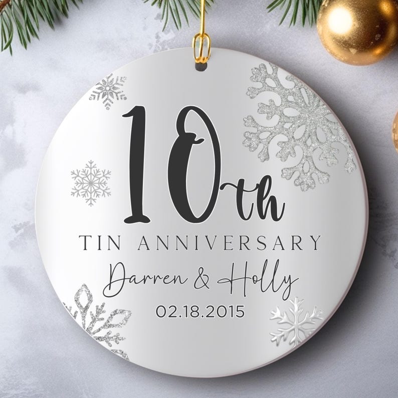 May include: White round Christmas ornament with a silver glitter snowflake design. The ornament features the text "10th Tin Anniversary Darren & Holly 02.18.2015".