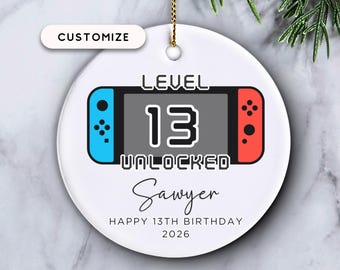 Può includere: Ornamento natalizio rotondo in ceramica bianca con un design a controller di videogiochi. L'ornamento recita "LEVEL 13 UNLOCKED", il nome "Sawyer" e "HAPPY 13TH BIRTHDAY 2026". Include un cordino dorato per appenderlo.