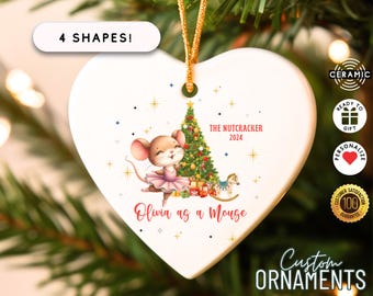 Può includere: Ornamento natalizio a forma di cuore in ceramica bianca con cordino dorato per appenderlo. Presenta un topo dei cartoni animati in tutù rosa, un albero di Natale e il testo "The Nutcracker 2024" e "Olivia as a Mouse". È presente anche il testo "4 Shapes".