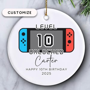 May include: White ceramic ornament with a video game controller design. The ornament features the text "LEVEL 10 UNLOCKED" and "Carter", with "HAPPY 10TH BIRTHDAY 2025" below. A gold string is attached for hanging.