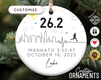 May include: A white round ceramic ornament featuring the text 26.2, a black skyline silhouette, a heartbeat line, and a running figure. Below, the text reads MANKATO 3:55:47, OCTOBER 18, 2025, and the name Luke in a script font.