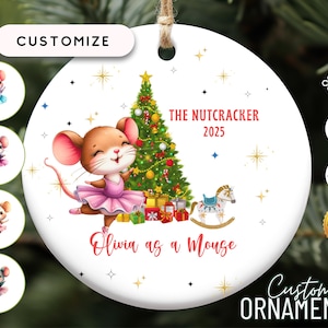 May include: A white ceramic Christmas ornament featuring a cartoon mouse in a pink tutu, a decorated Christmas tree, and the text "The Nutcracker 2025". The ornament is personalized with the text "Olivia as a Mouse".