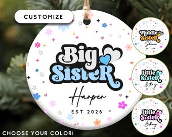 May include: A white ceramic ornament with the words "Big Sister" in a retro font, the name "Harper", and the year "EST 2026". The ornament is decorated with colorful flowers and stars. Additional options include "Middle Sister" and "Little Sister" designs.