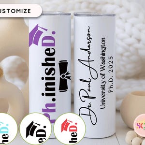May include: Two white stainless steel tumblers. One features the text "ph.inished D." with a purple graduation cap graphic. The other tumbler has the name "Dr. Paul Anderson", University of Washington, and "Ph.D. 2025".